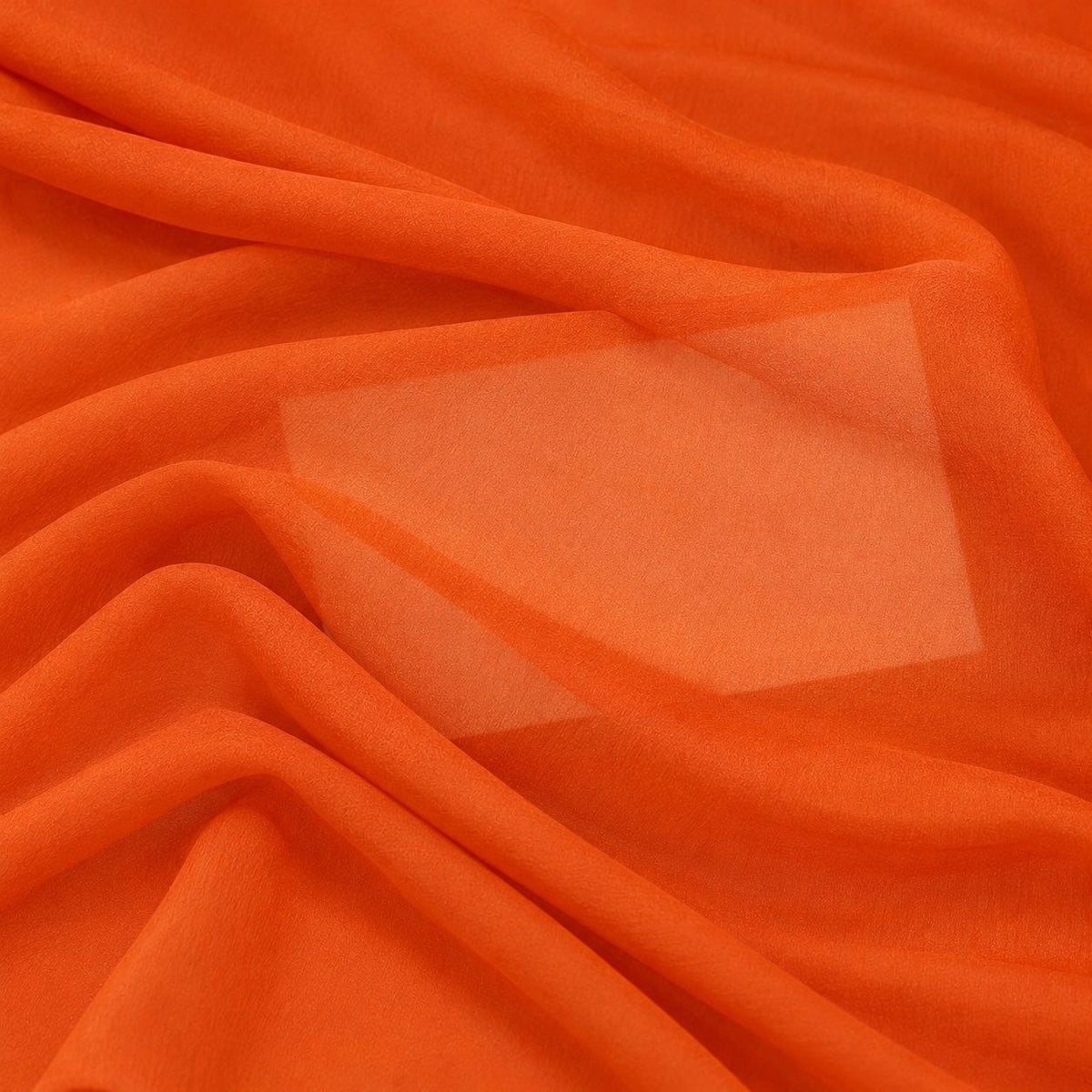 Orange silke georgette – nærbillede med papir bag stoffet, der viser at det kun er svagt gennemsigtigt (billede 3 af 3)