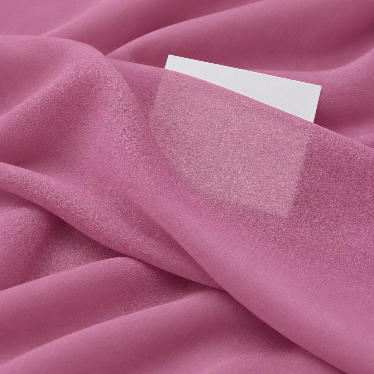 Støvet rosa silke georgette – nærbillede med papir bag stoffet, der viser at det kun er svagt gennemsigtigt (billede 3 af 3)