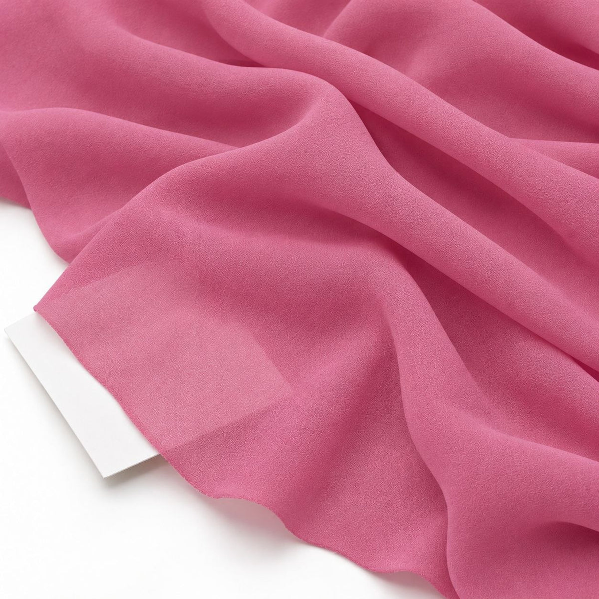 Rosa silke georgette – nærbillede med papir bag stoffet, der viser at det kun er svagt gennemsigtigt (billede 3 af 3)
