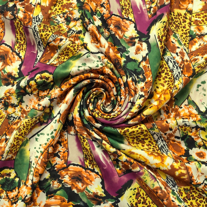 MØNSTRET POLYESTERSTOF – GUL/ORANGE/LILLA MULTI – stoffet samlet i en blød swirl, med printet synligt (billede 1 af 3)
