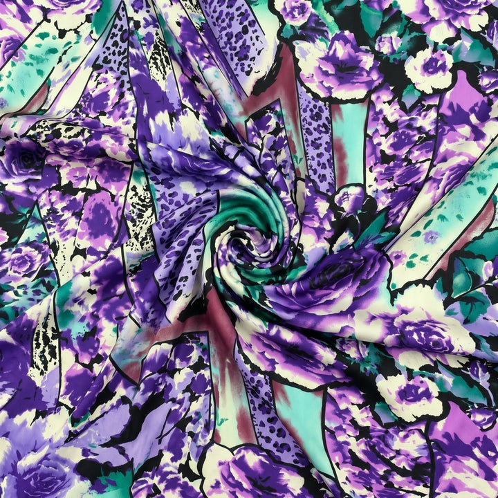 MØNSTRET POLYESTERSTOF – LILLA/TURKIS MULTI – stoffet samlet i en blød swirl, med printet synligt (billede 1 af 3)