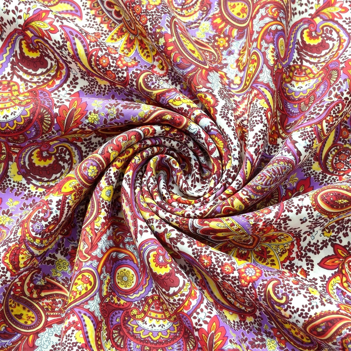 PAISLEY POLYESTERSTOF – LILLA/GUL/RØD MULTI – stoffet samlet i en blød swirl, med printet synligt (billede 1 af 3)